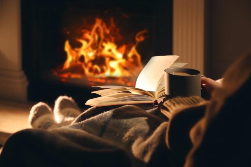 woman with cup of drink and book near fire place at